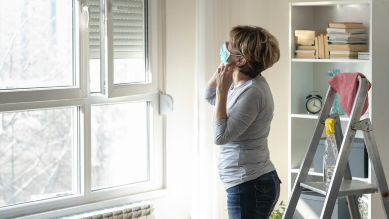 fukt, sopp, muggsopp, råte - kvinne med munnbind ser på et vindu