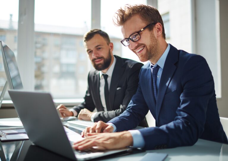 utbetaling av utbytte - to menn som smiler foran en datamaskin